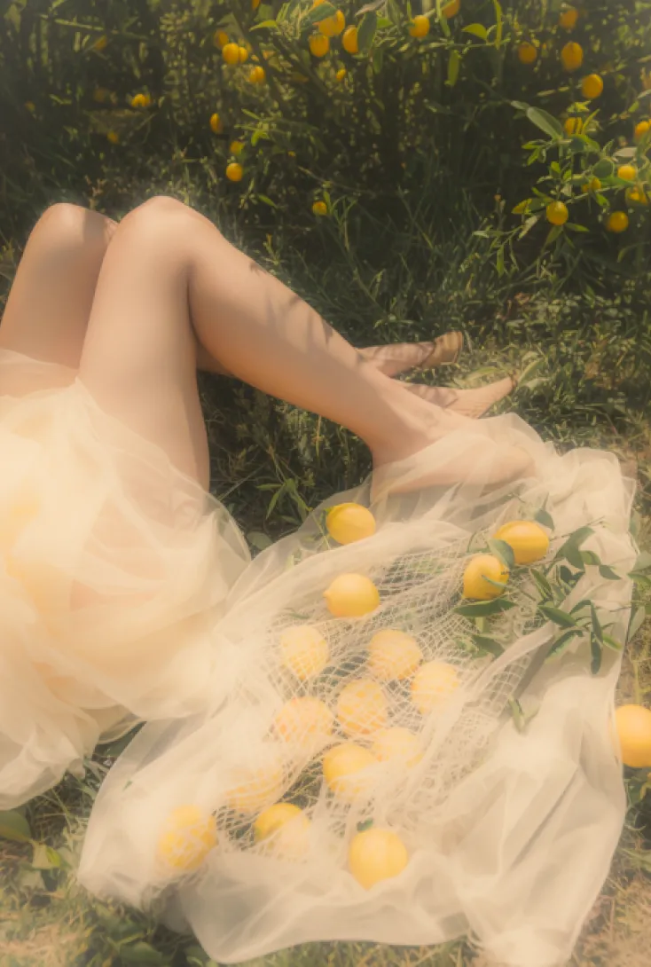 Image of a girl lying in the field  with lemons by her side edited  with Lensa dreamy filter